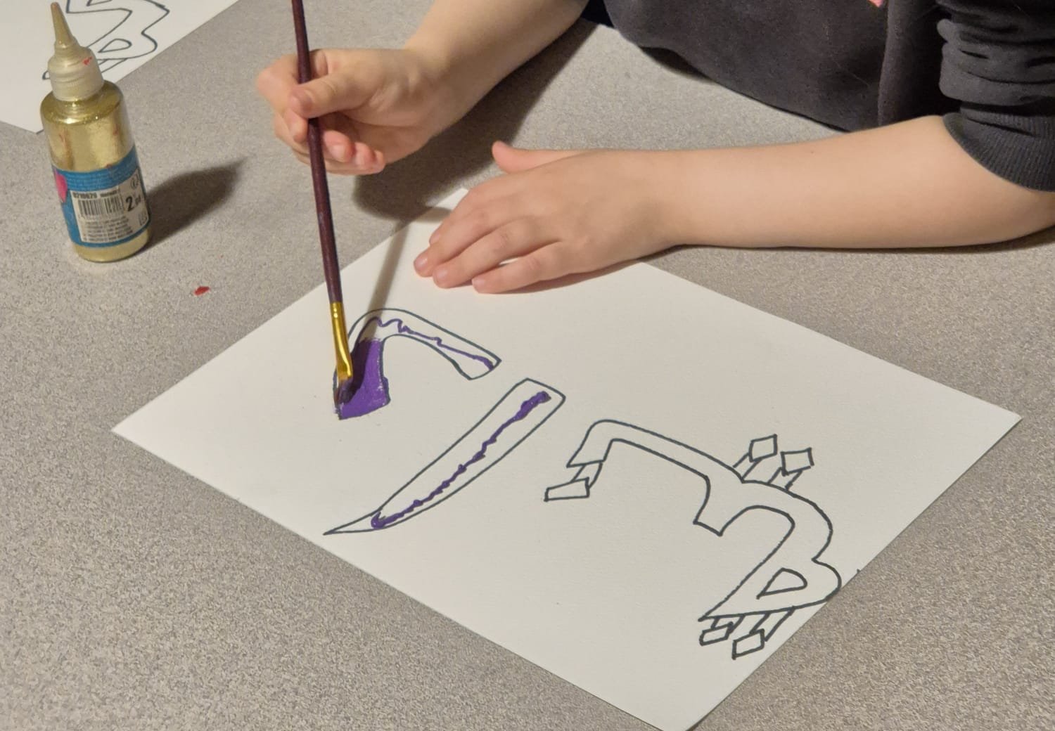 Enfant qui peint des lettres arabes au pinceau